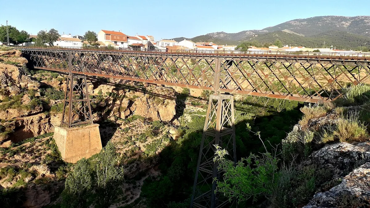 Puente de hierro sobre un barranco con casas al fondo